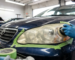 Technician polishing cloudy car headlight taped off with green painter's tape