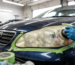 Technician polishing cloudy car headlight taped off with green painter's tape
